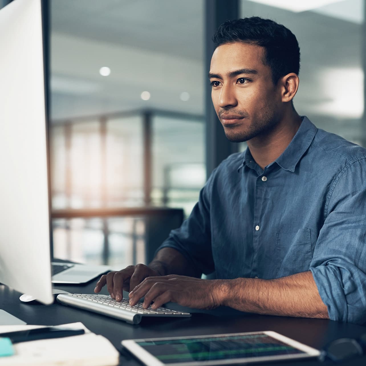 A man sitting at a desk, using a laptop computer in an office setting.